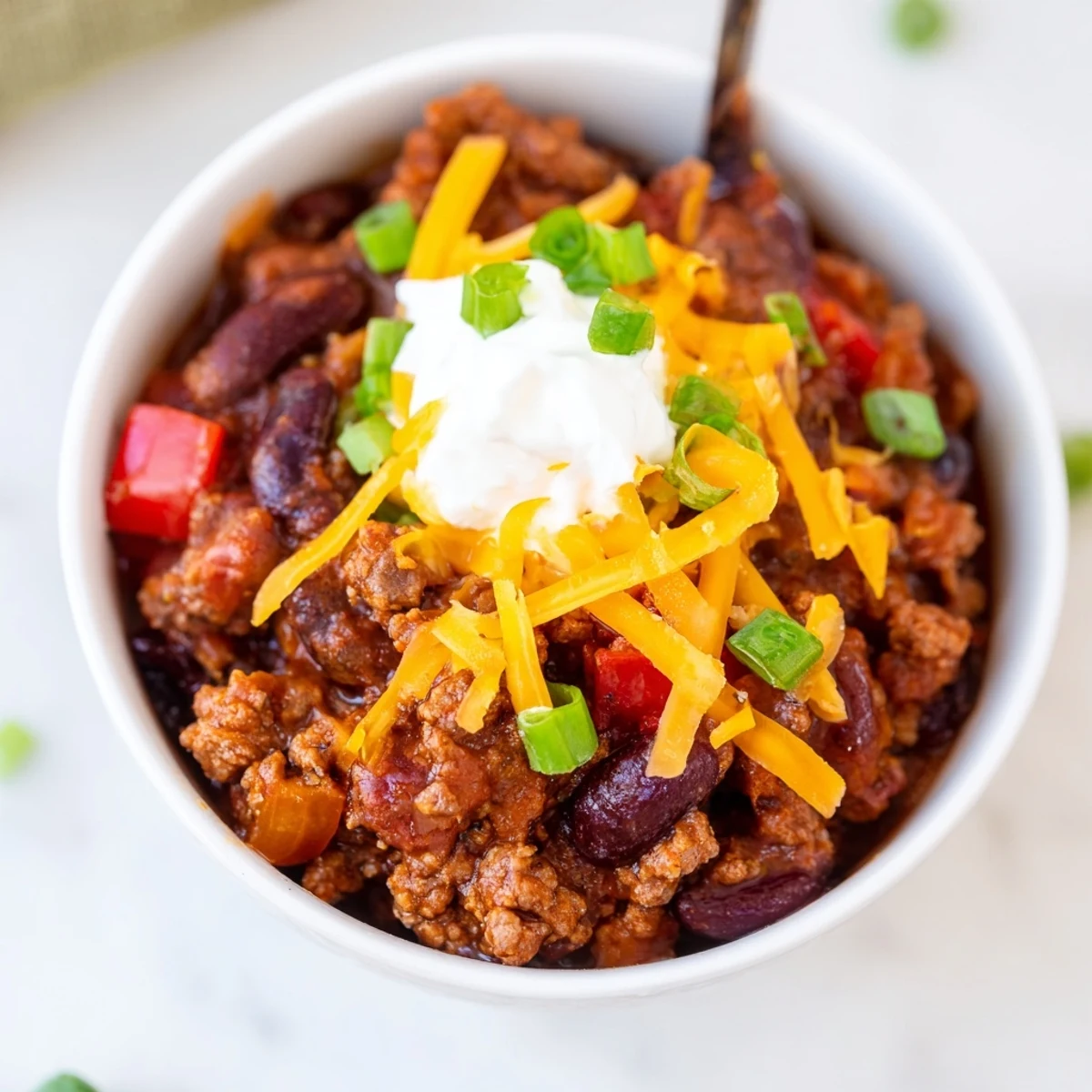 Red Dutch oven pot filled with rich Beef and Bean Chili with Sharp Cheddar and a dollop of sour cream.