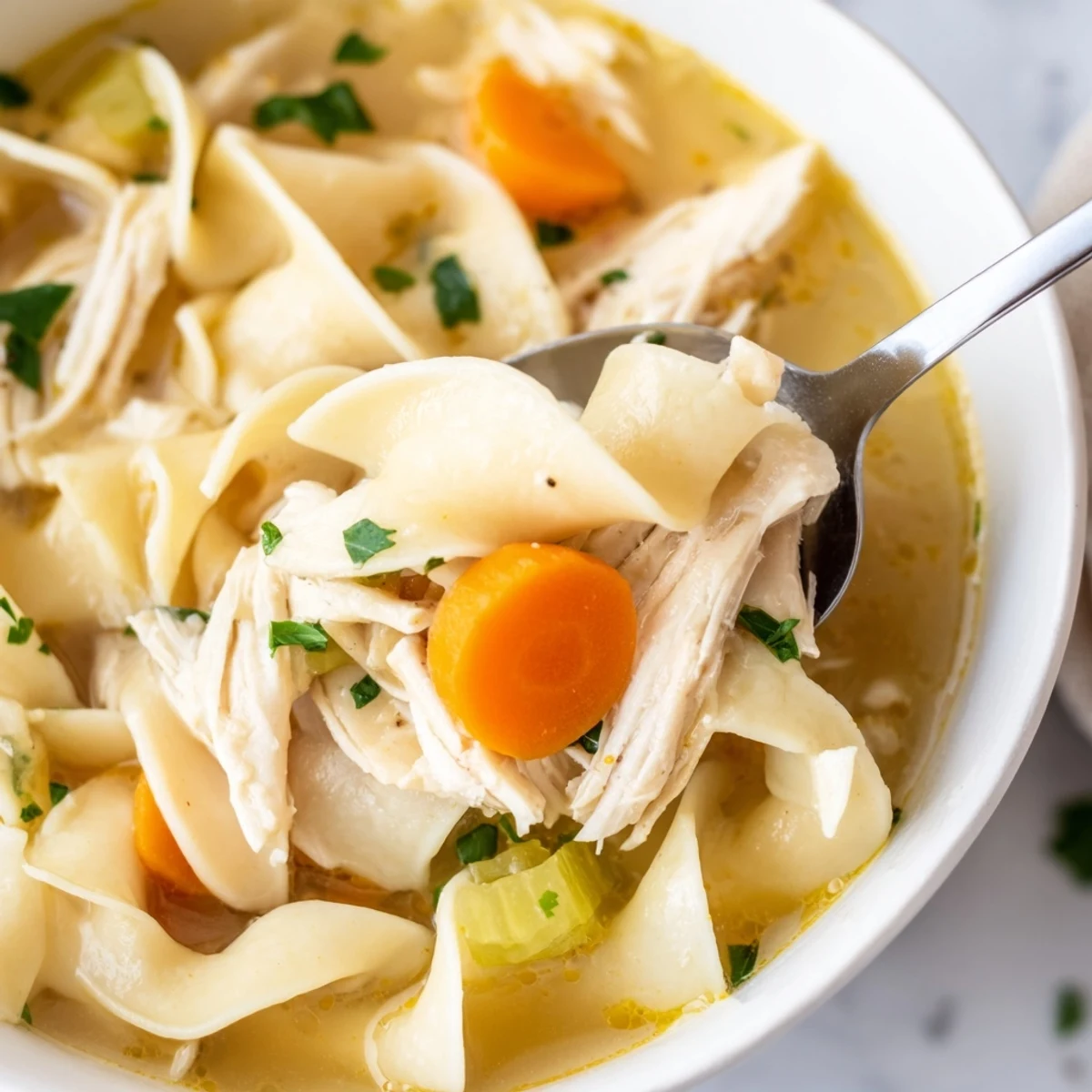 Steaming bowl of Chicken Noodle Soup with Homemade Noodles, featuring tender chicken, carrots, and celery in a rich golden broth.