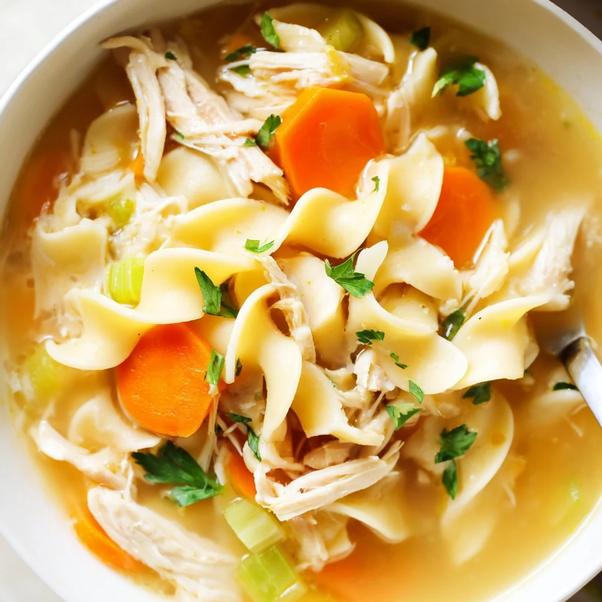 Close-up of Chicken Noodle Soup with Homemade Noodles, showing silky noodles, diced chicken, and vibrant vegetables in a savory broth.