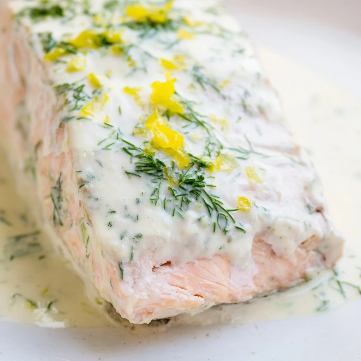 Golden-brown baked salmon fillets topped with creamy dill and lemon sauce, served on a white plate.