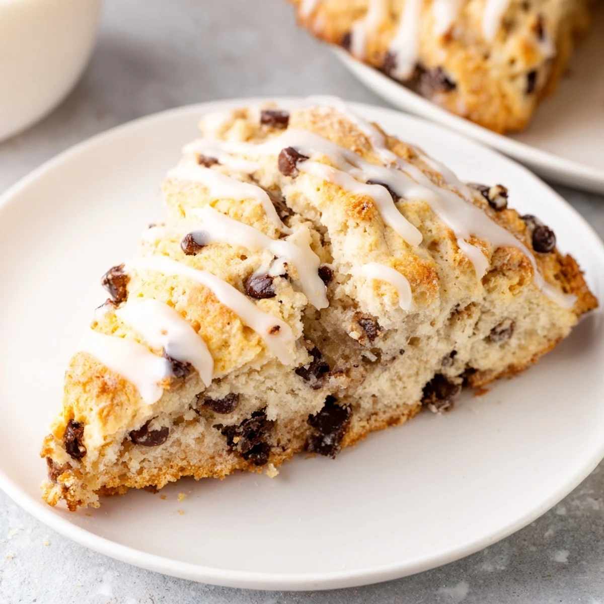 A close-up view of a Chocolate Chip Scone with Sweet Vanilla Glaze showing a flaky interior and melting chocolate chips.