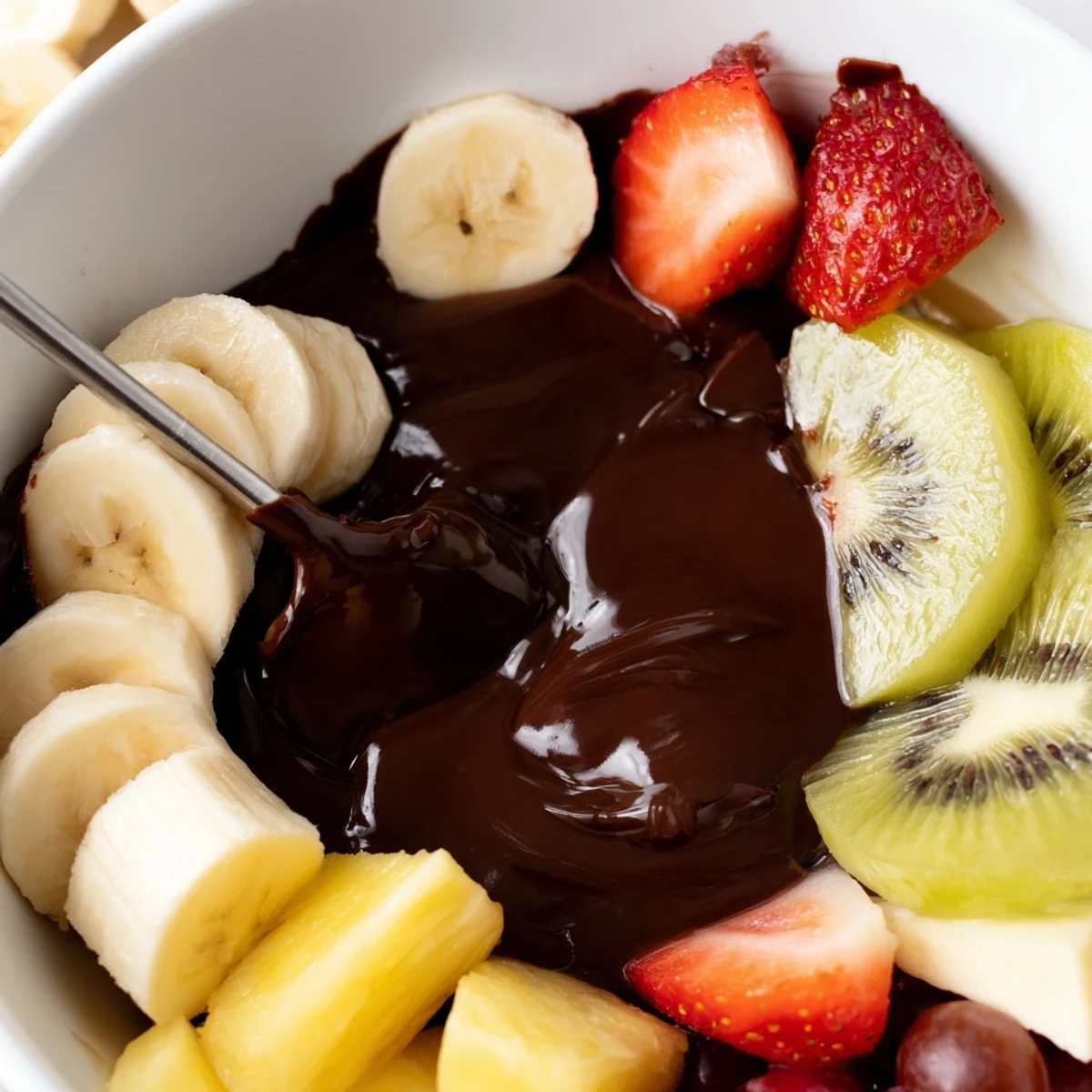 Valentine Chocolate Fondue with Fresh Fruit sits in a ceramic pot beside a platter of ripe pineapple and grapes, ready for a cozy romantic dessert at home.  
