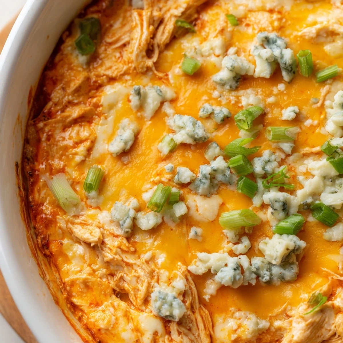 Golden, bubbly Spicy Buffalo Chicken Dip in a white dish, surrounded by crispy tortilla chips for dipping.
