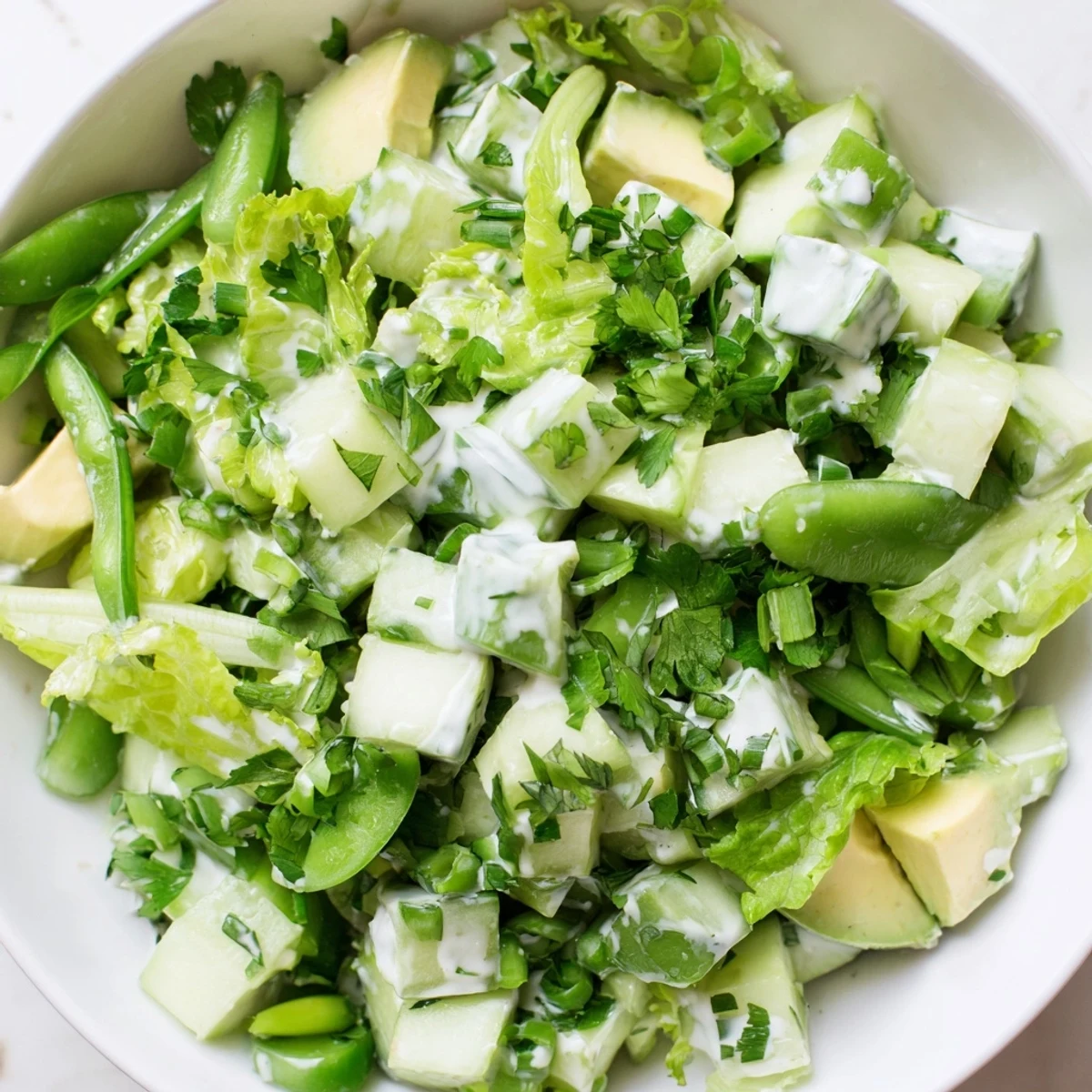 A close-up of the vibrant Green Goddess Salad with Cucumber and Avocado, showing crisp cucumber pieces and creamy avocado chunks nestled among leafy greens.