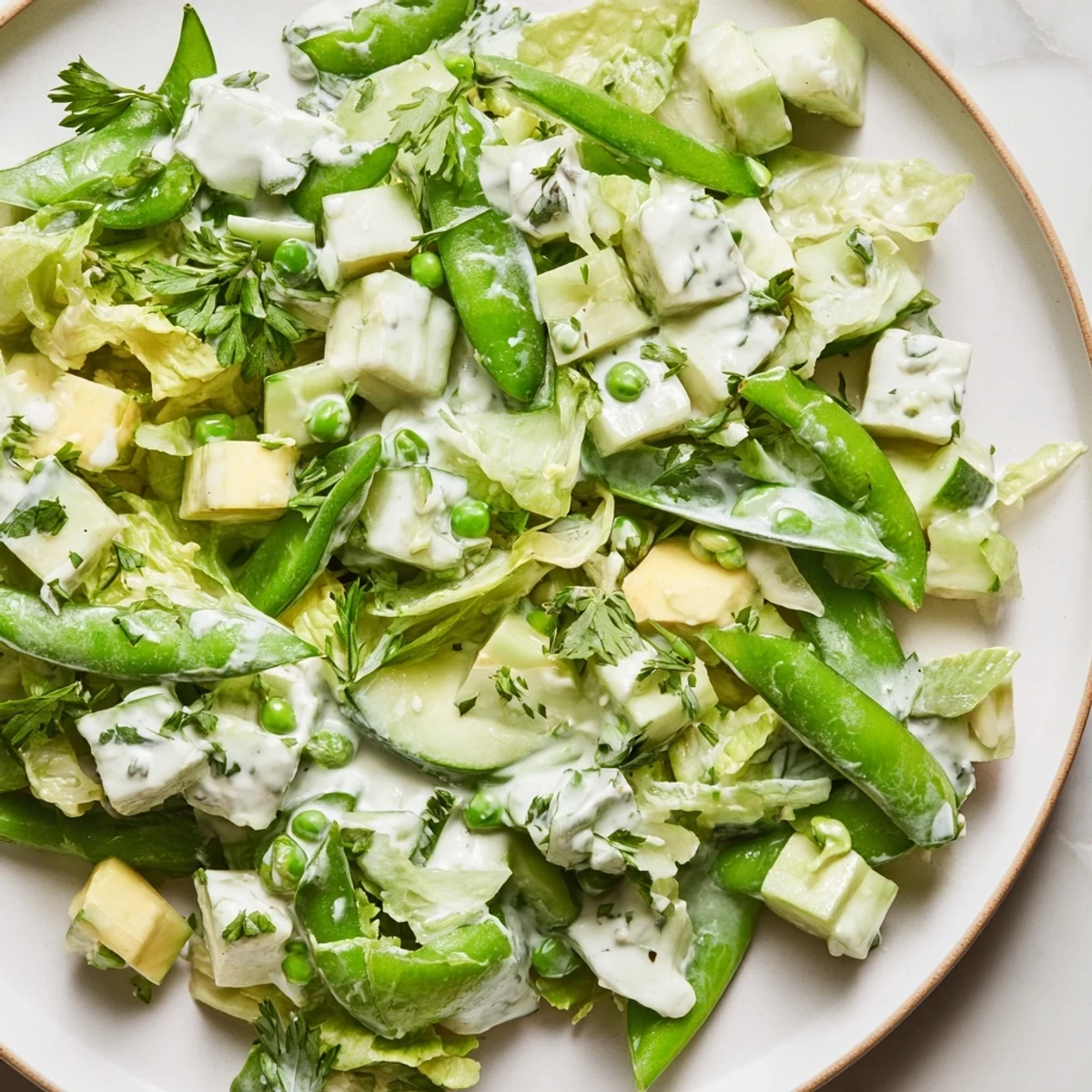 Freshly tossed Green Goddess Salad with Cucumber and Avocado, drizzled with herby dressing and garnished with chopped parsley and chives for a colorful presentation.