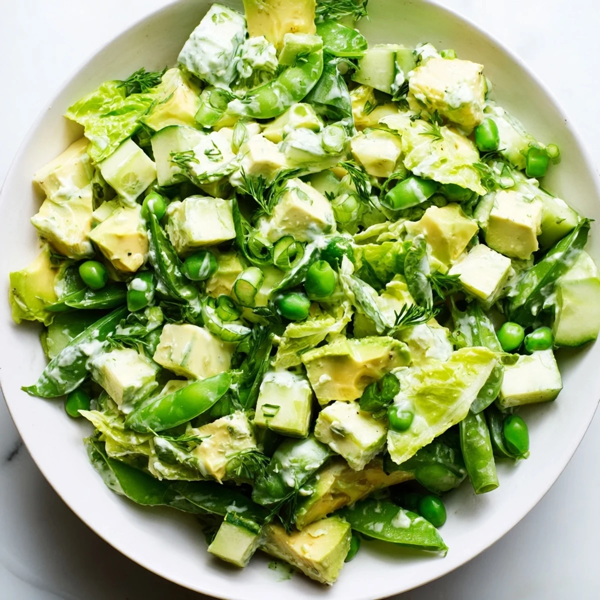 A serving bowl of the Green Goddess Salad with Cucumber and Avocado, highlighting the bright green dressing coating the vegetables and ripe avocado slices.