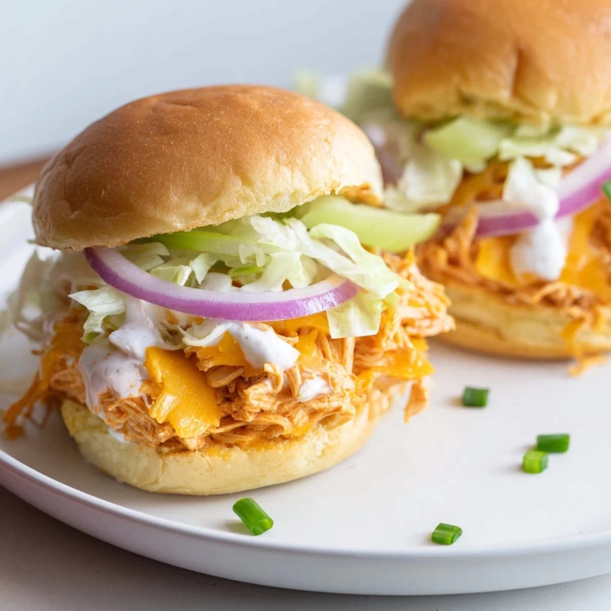 Golden Buffalo Chicken Sliders with Ranch Dressing are served on soft buns, topped with crisp lettuce and creamy drizzle for a party snack.  