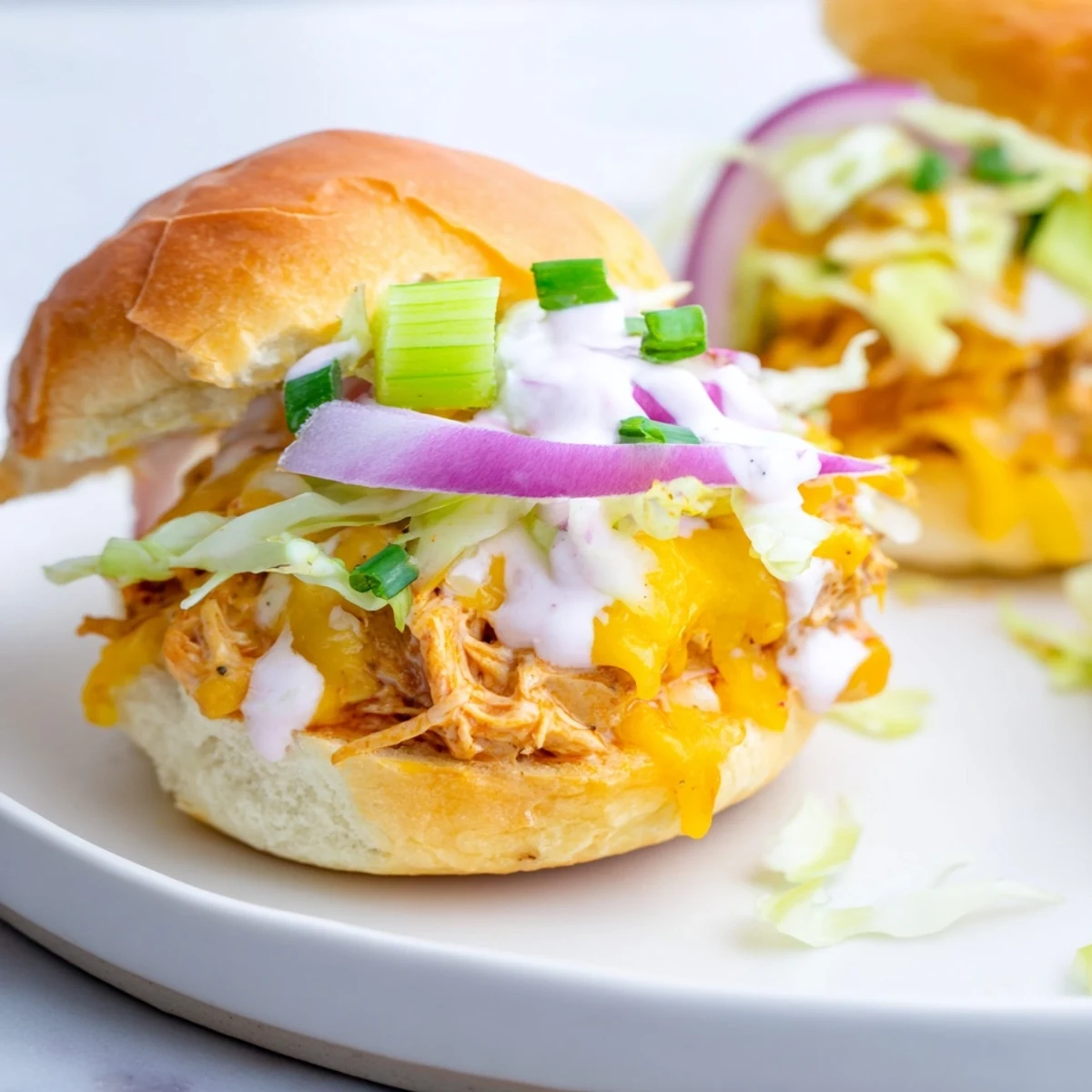 A close-up of Buffalo Chicken Sliders with Ranch Dressing highlights shredded chicken, fresh lettuce, and a generous drizzle of ranch on the buns.