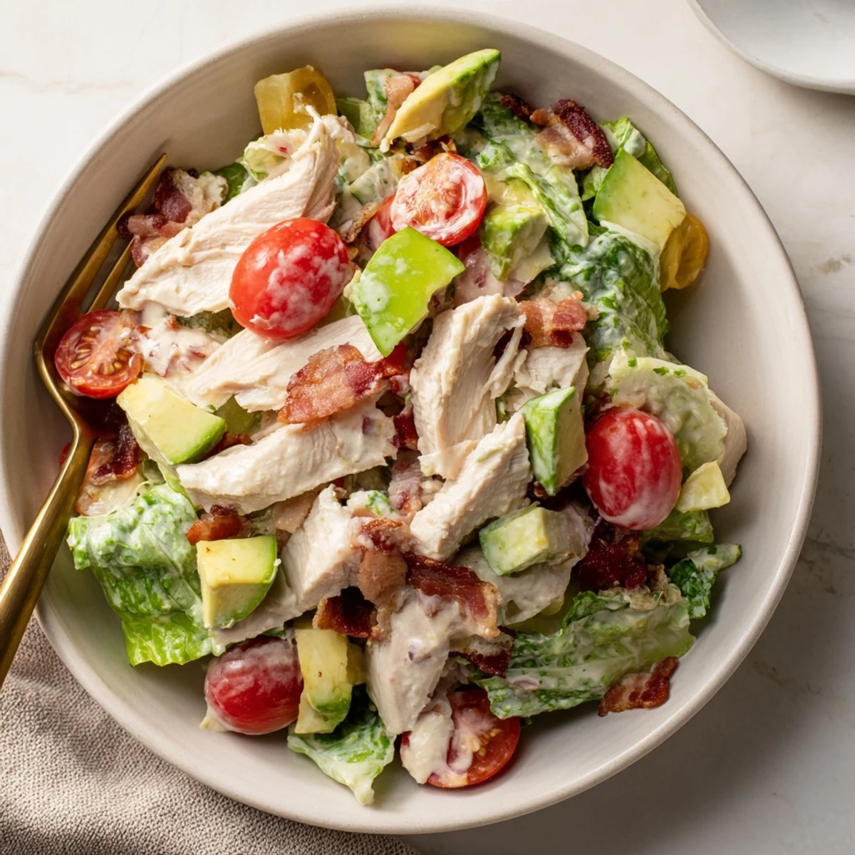 Freshly cooked BLT Chicken Salad with crispy bacon crumbles and juicy tomato slices on a bed of chopped romaine lettuce.