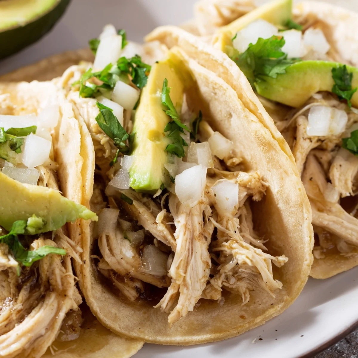 Chicken Street Tacos served on a plate with charred corn tortillas, avocado slices, cilantro, onion, and zesty lime wedges.