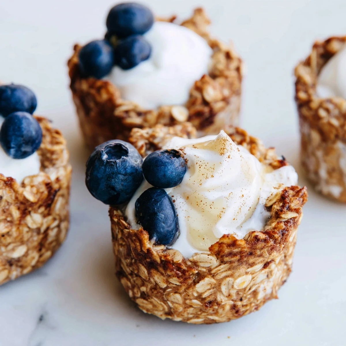 Golden-baked oatmeal cups with creamy Greek yogurt topping, fresh berries, and a drizzle of honey on a wooden board.