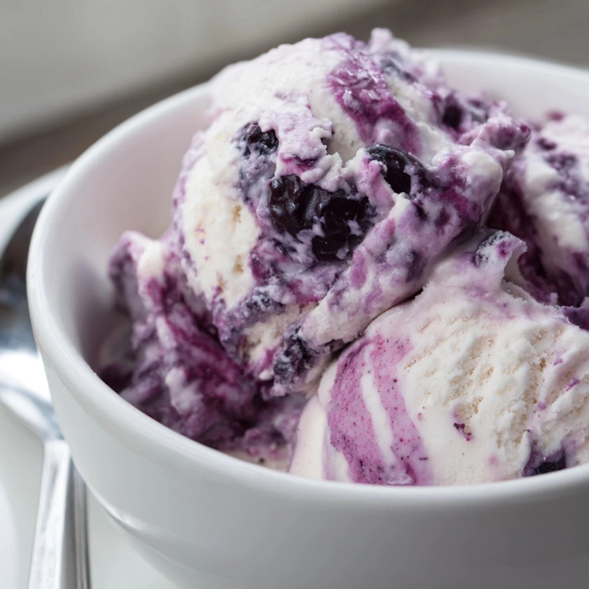 Scoops of Blueberry Cottage Cheese Ice Cream in a bowl, creamy swirl with blueberry specks and honey drizzle, summer dessert idea.