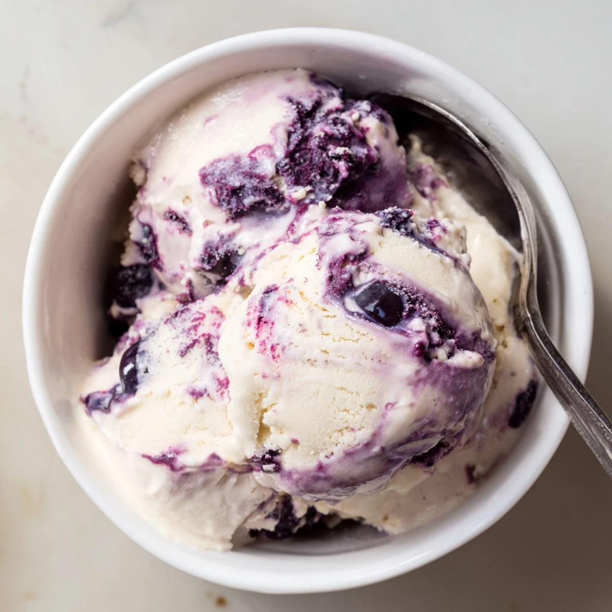 A close-up of Blueberry Cottage Cheese Ice Cream in a cone, showing smooth texture, fresh blueberries, and a mint garnish for serving.