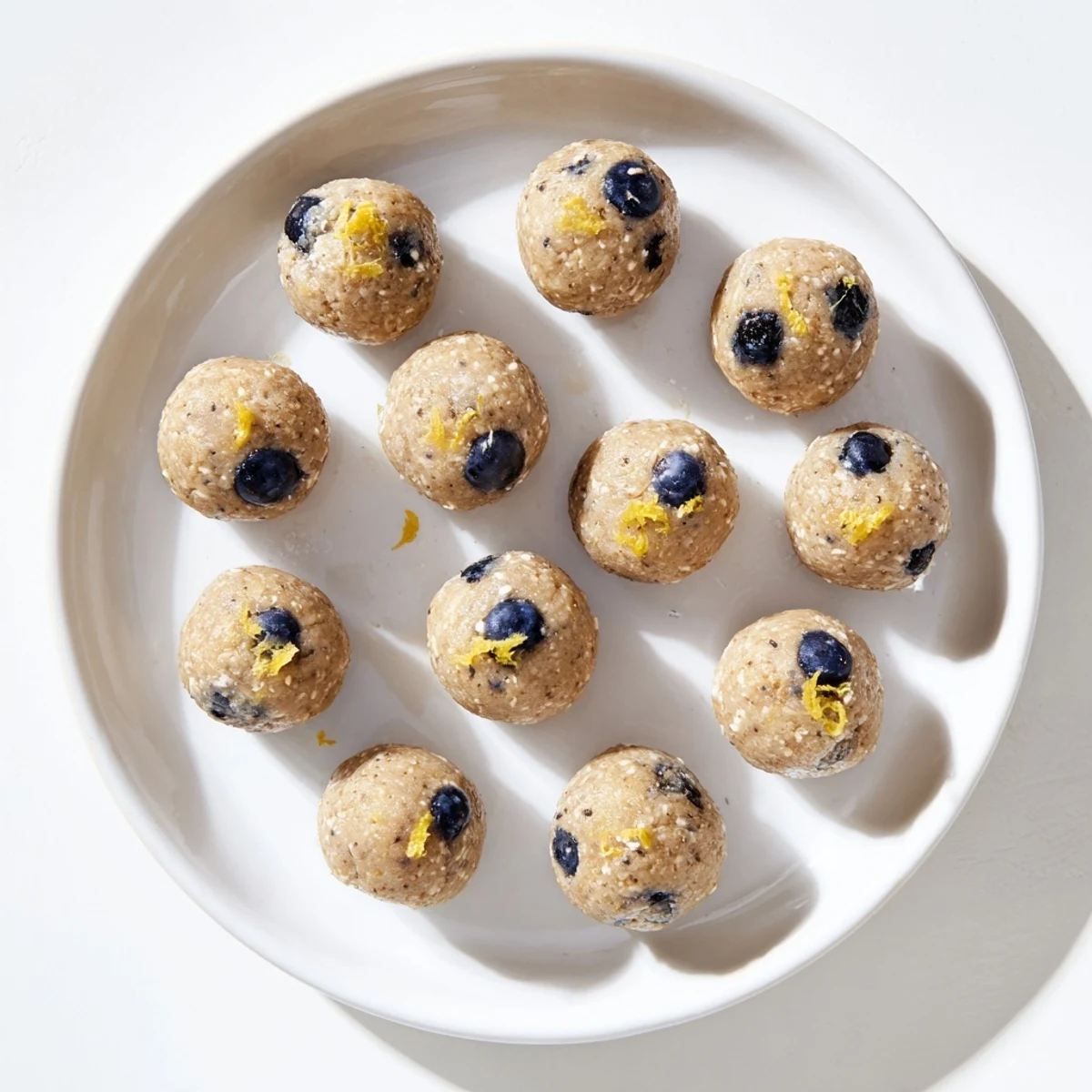 Fresh blueberries and a sweet glaze top these no-bake Blueberry Cheesecake Protein Bites on parchment.