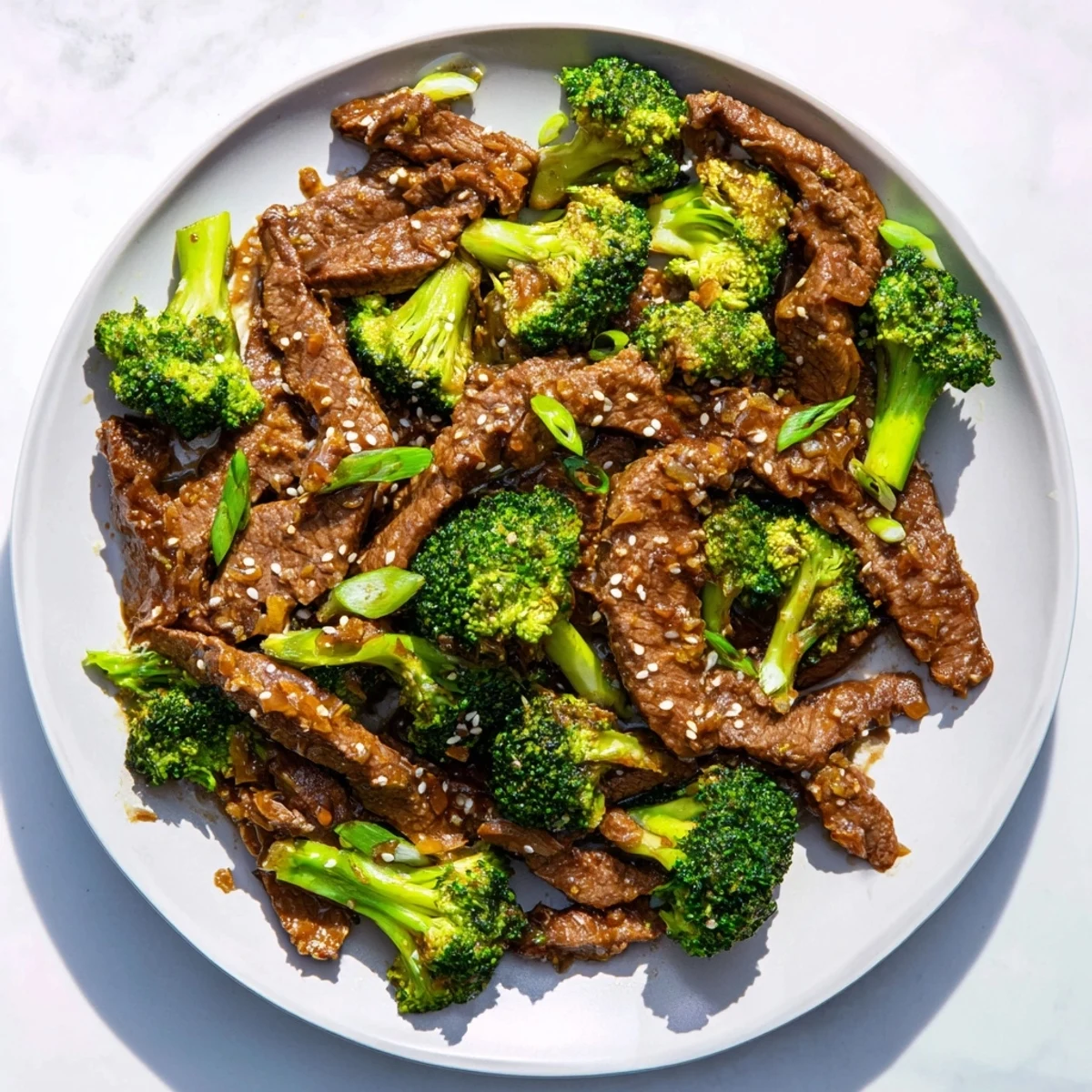Better Than Takeout Beef With Broccoli on a white plate with sesame seeds and fresh green onions.