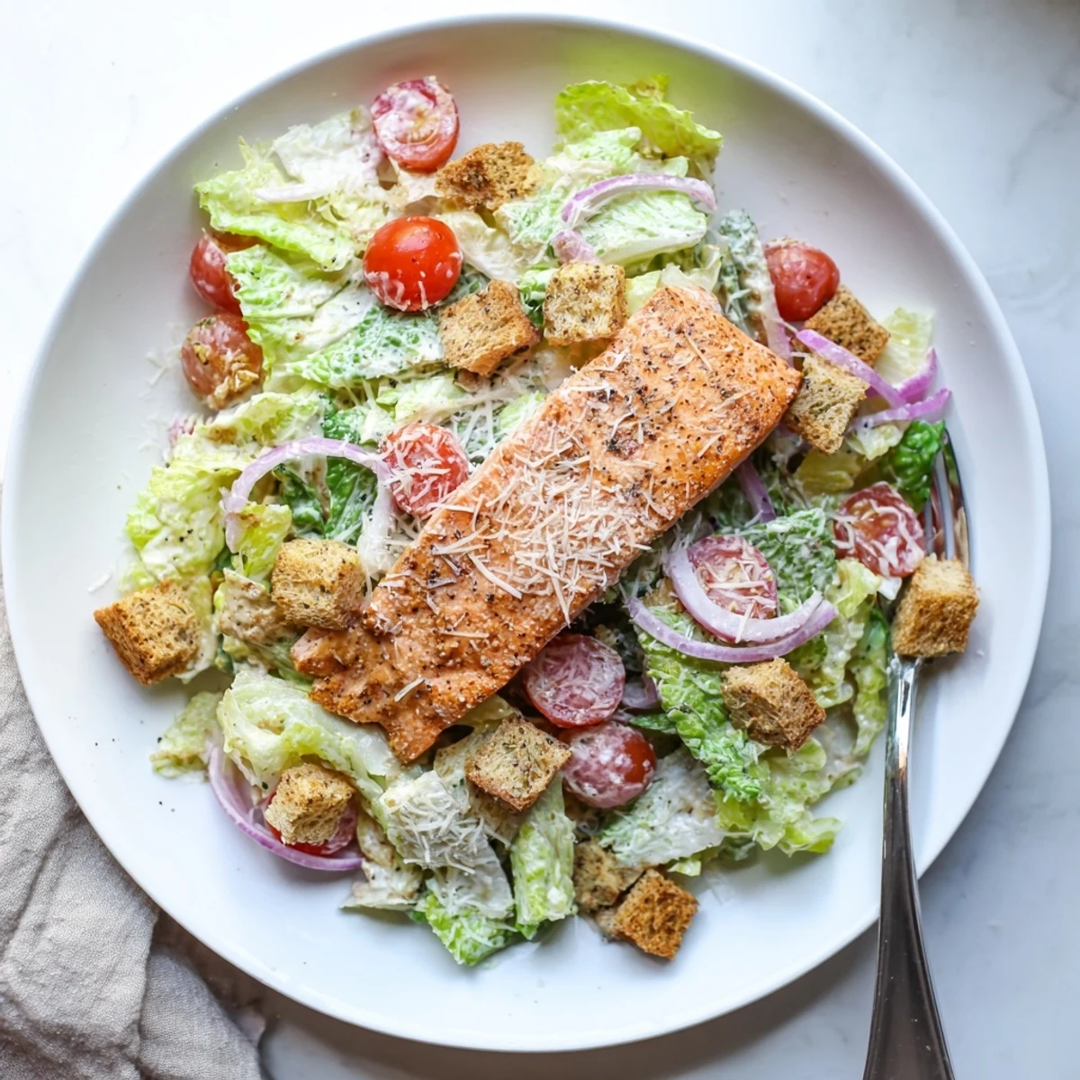 Freshly grilled salmon fillet rests atop a vibrant salad of crisp romaine, crunchy croutons, and halved cherry tomatoes.