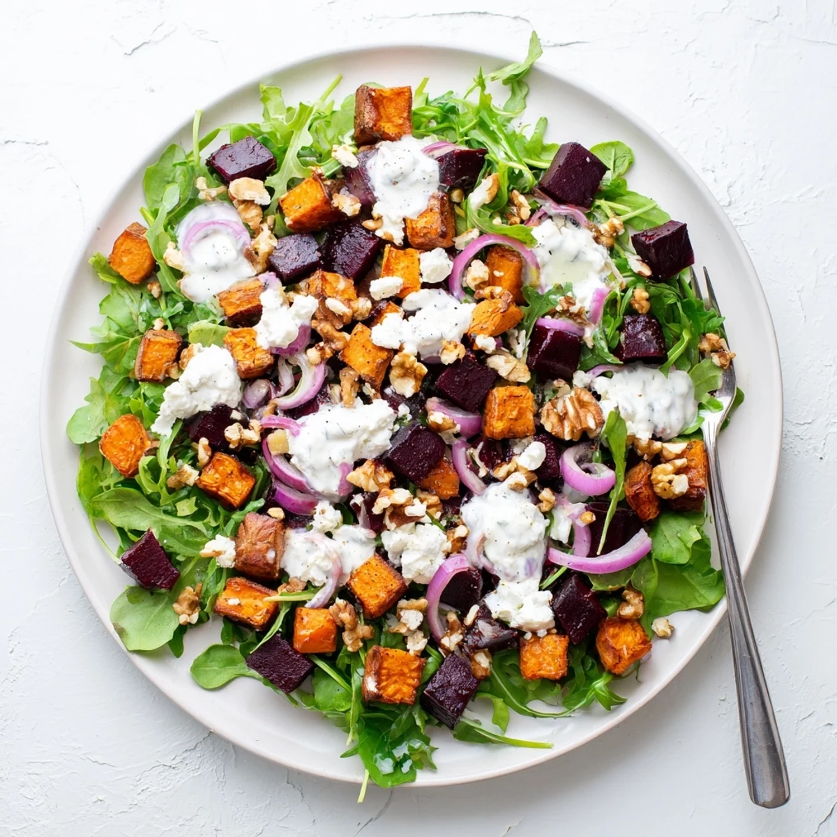 Golden roasted beets and sweet potatoes topped with crumbled feta and creamy yogurt dressing in a vibrant salad bowl