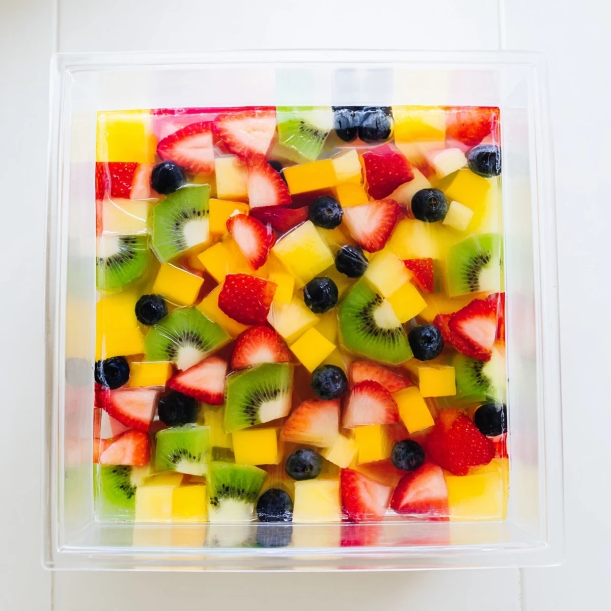 Vegan-friendly agar agar fruit jelly cube topped with fresh blueberries and pineapple on white serving plate