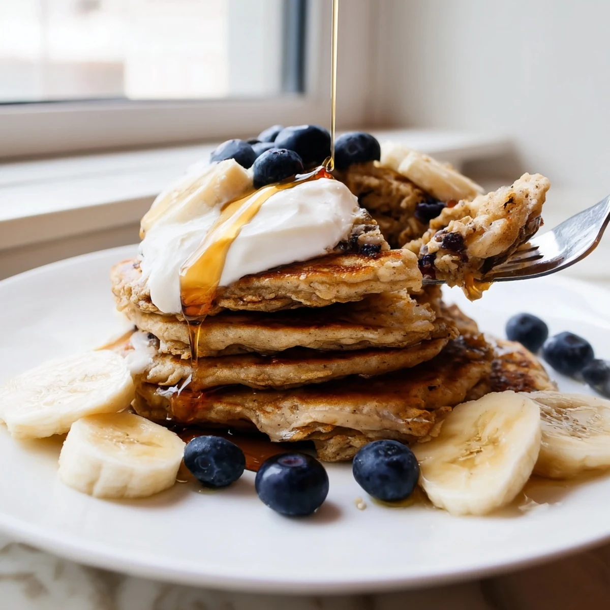 Warm banana oatmeal pancakes plated with Greek yogurt and sliced banana on a rustic background
