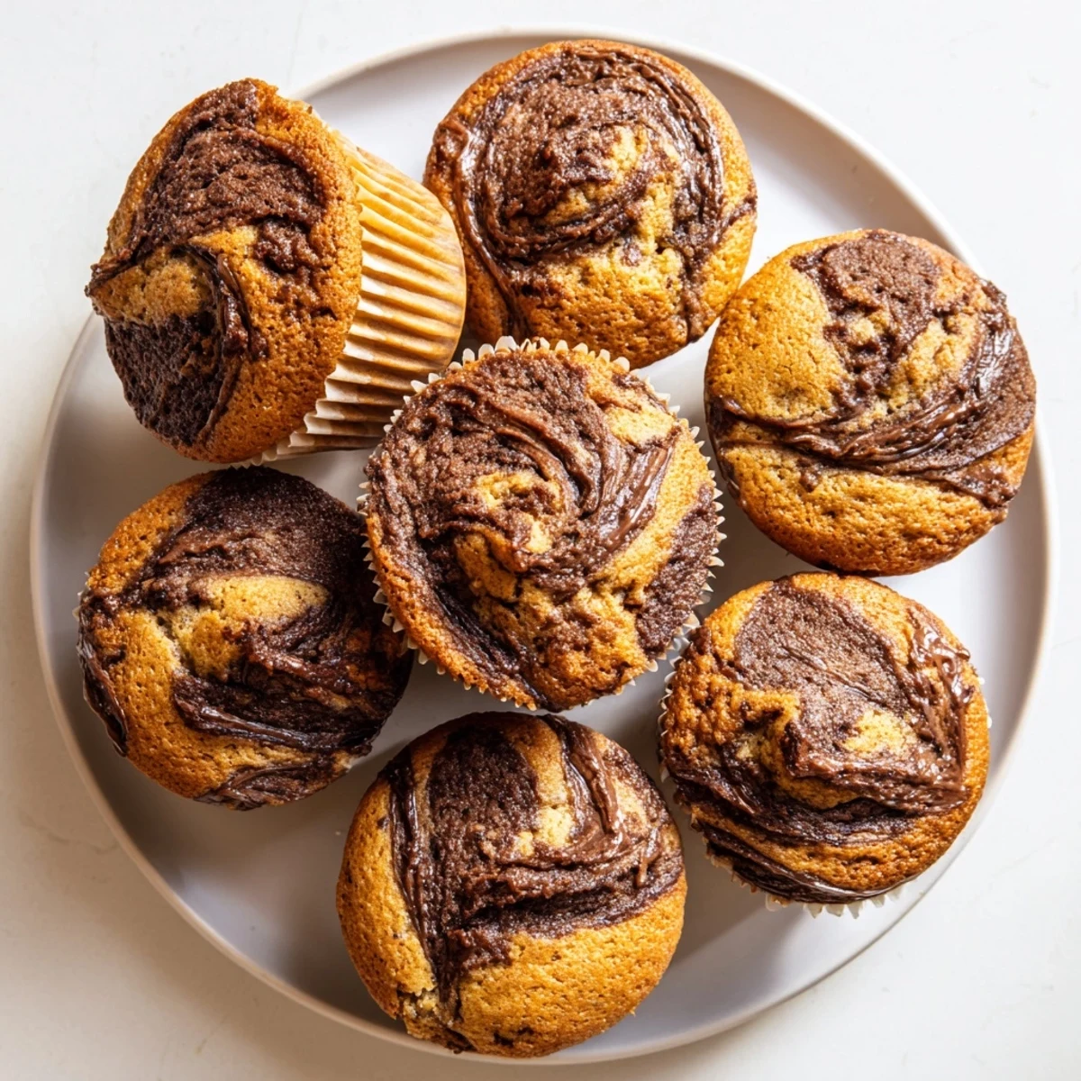 Freshly baked Nutella banana swirl muffins with golden tops and chocolate hazelnut ribbons swirling through tender banana bread