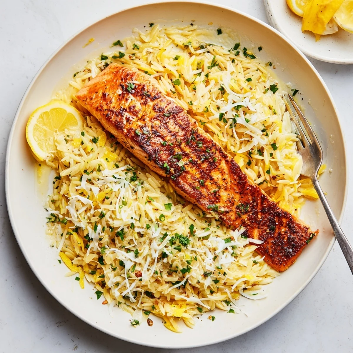 Golden pan-seared salmon fillets resting atop creamy lemon orzo with fresh parsley garnish