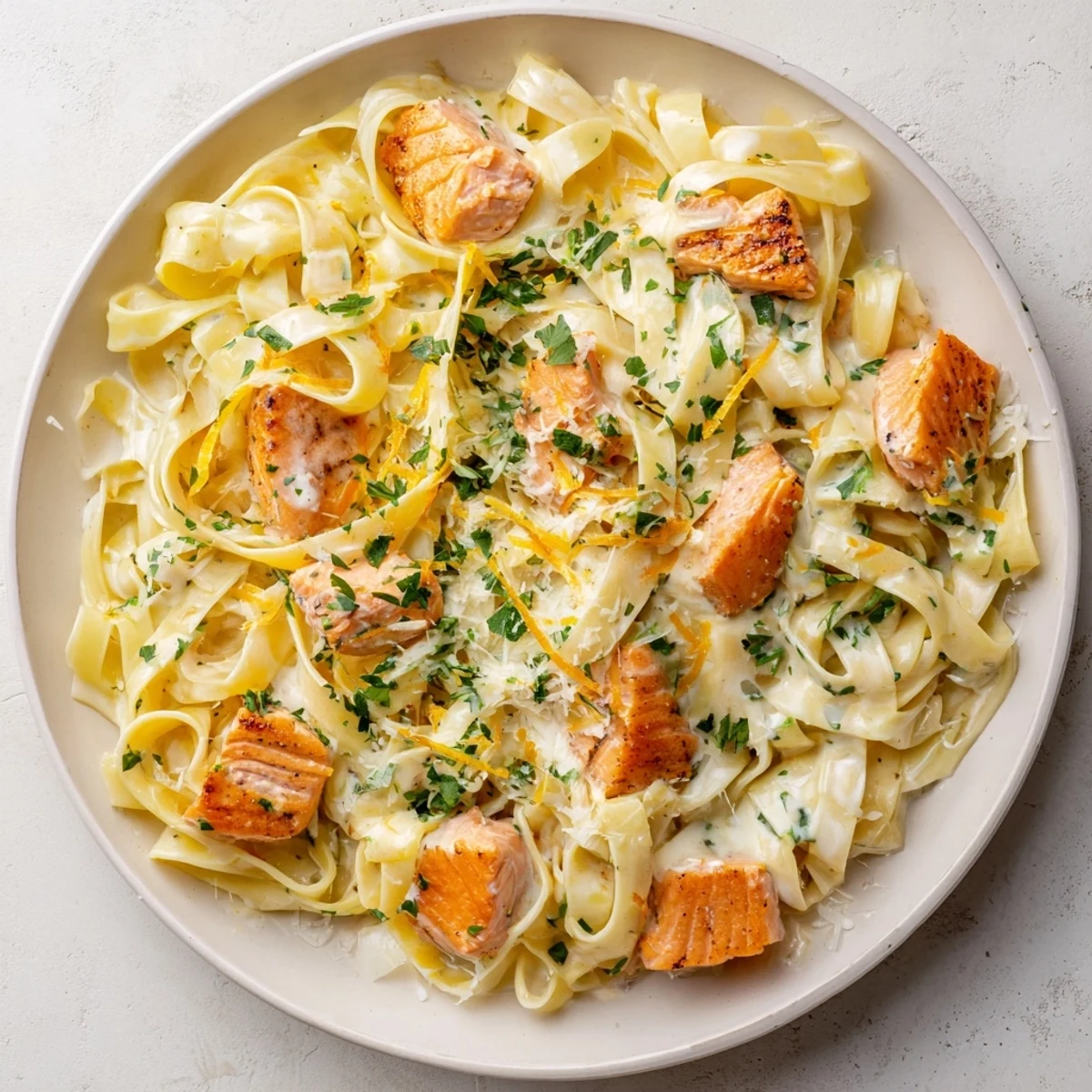 Golden seared salmon flakes resting atop fettuccine coated in a velvety garlic butter cream sauce