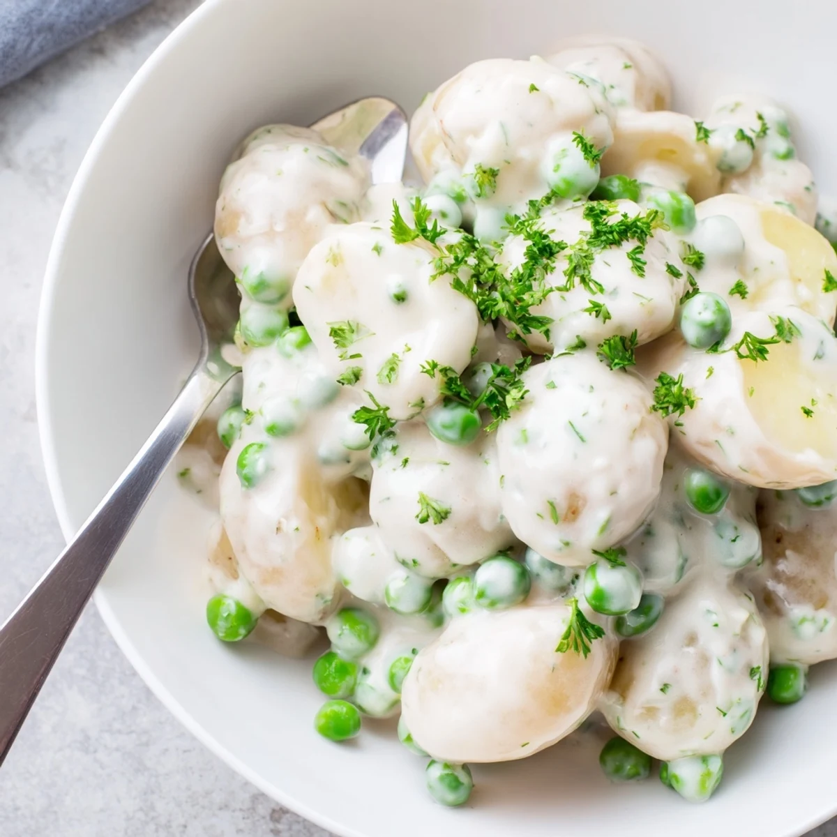 Golden creamed peas and potatoes in a white ceramic bowl topped with fresh green parsley garnish