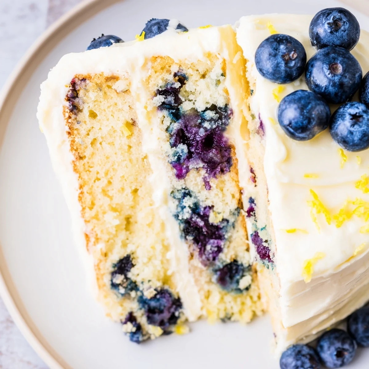 Moist lemon blueberry cake layered with creamy lemon cream cheese frosting and fresh blueberry garnish