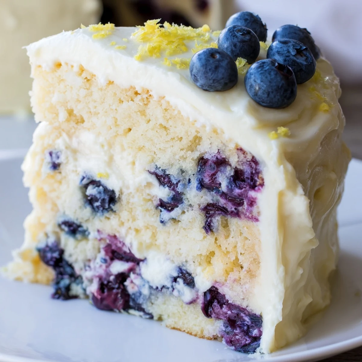 Slice of lemon blueberry cake on white plate showing tender crumb studded with purple blueberries