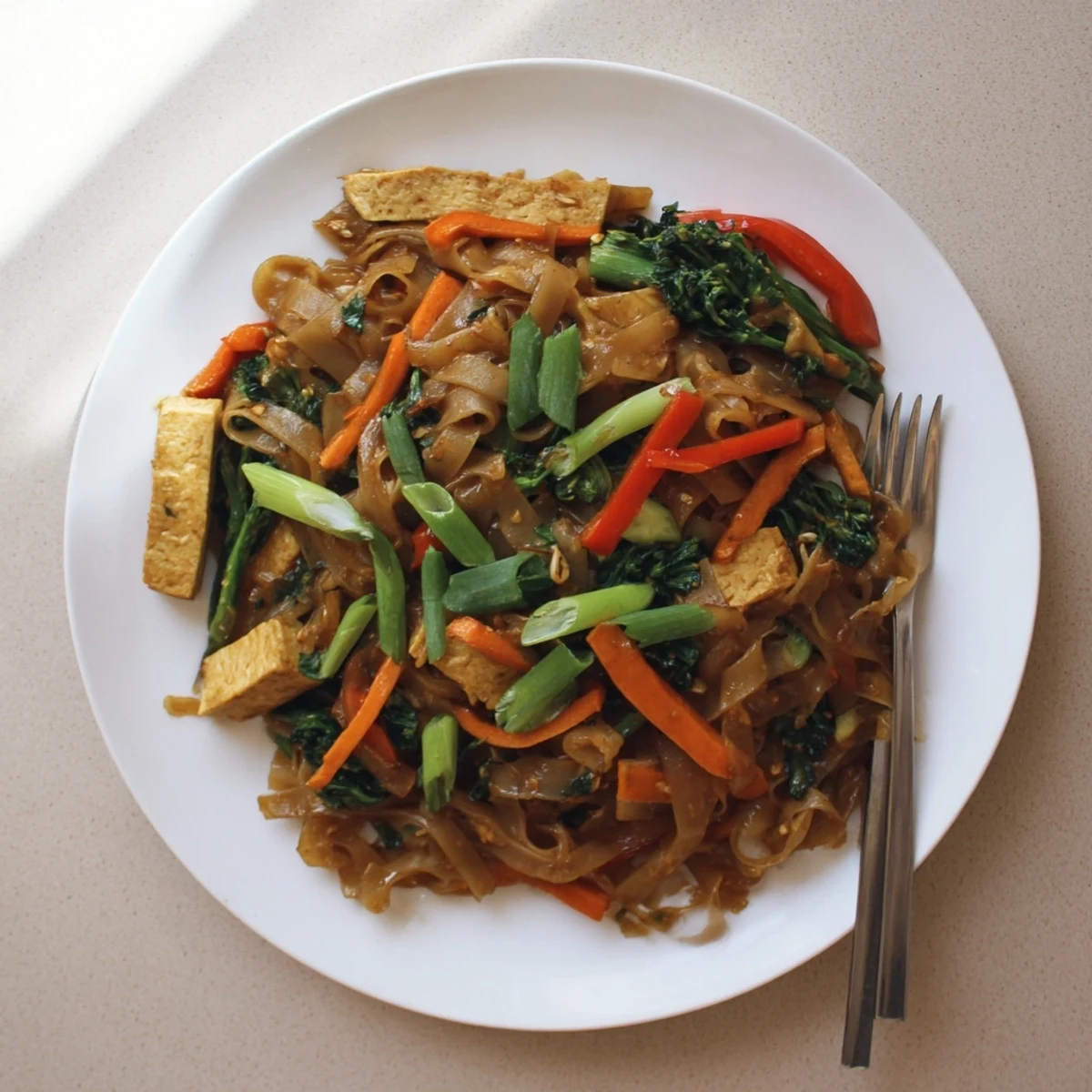 Steaming plate of Vegan Pad See Ew with tender rice noodles, gai lan, and fresh green onion garnish