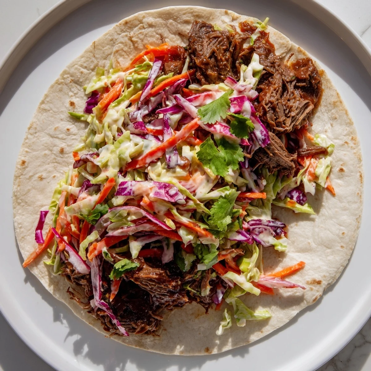 Close-up of shredded beef in sweet smoky BBQ sauce wrapped in soft tortilla with cabbage slaw