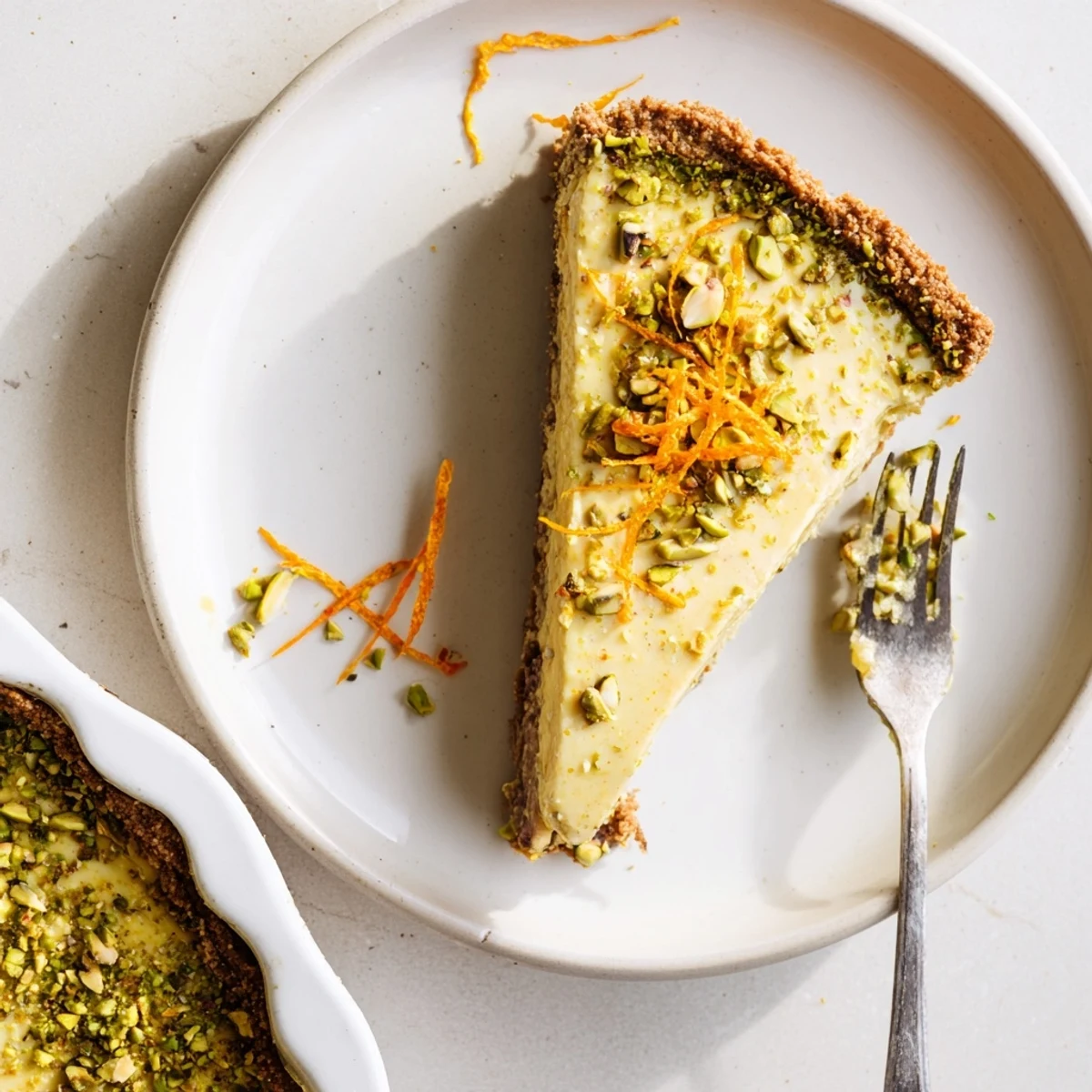 Orange cardamom tart showcasing creamy citrus filling in a golden pistachio crust garnished with chopped nuts