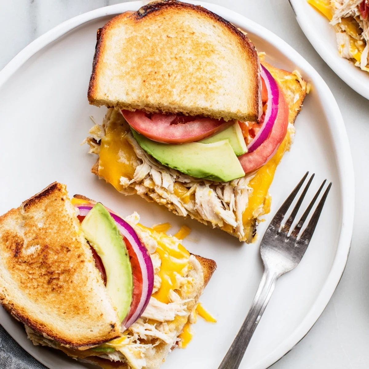 Sliced chicken avocado melt sandwich served warm on a plate with ripe avocado and melted cheddar cheese