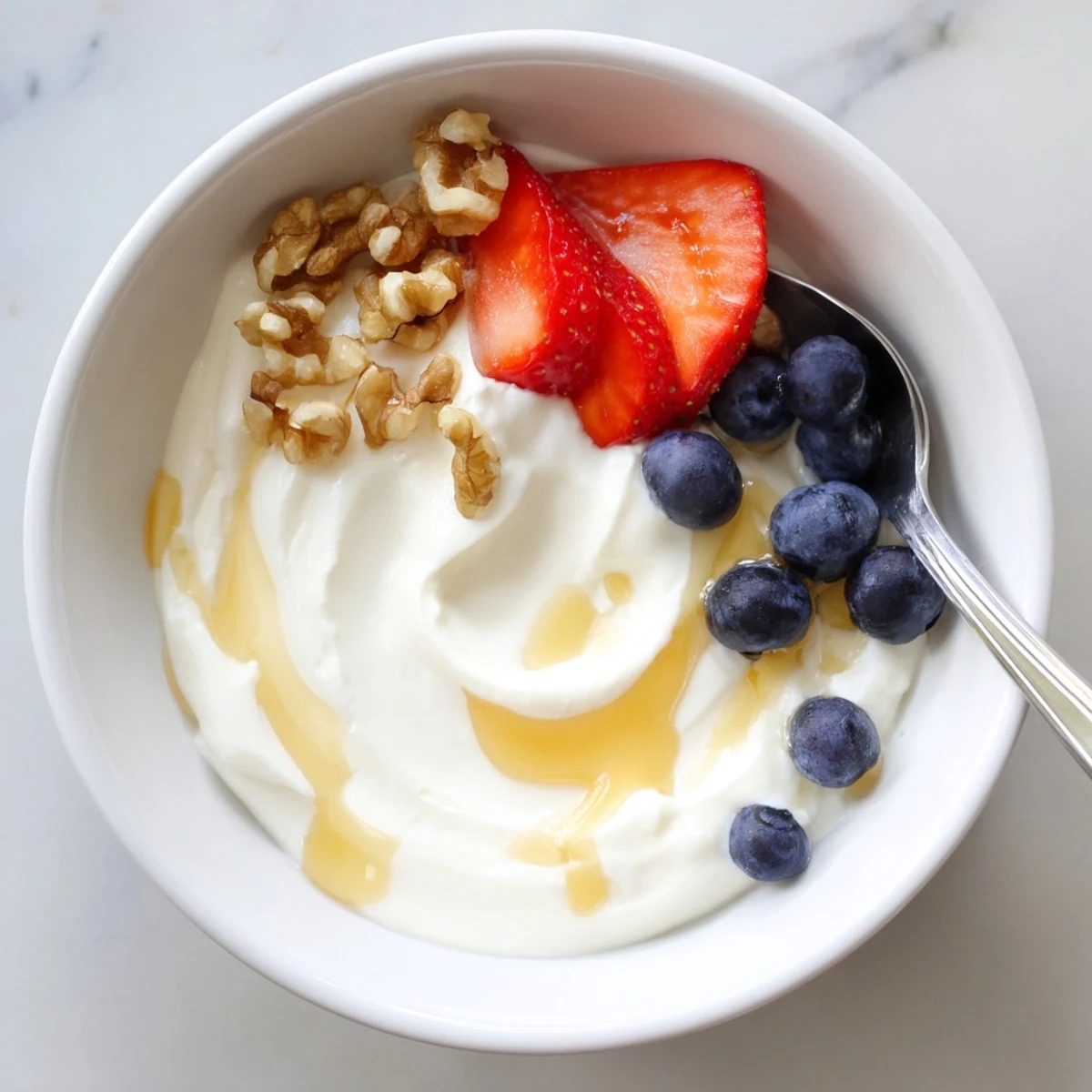 Thick Greek yogurt spoon dripping onto rustic wooden board with scattered nuts and fruit