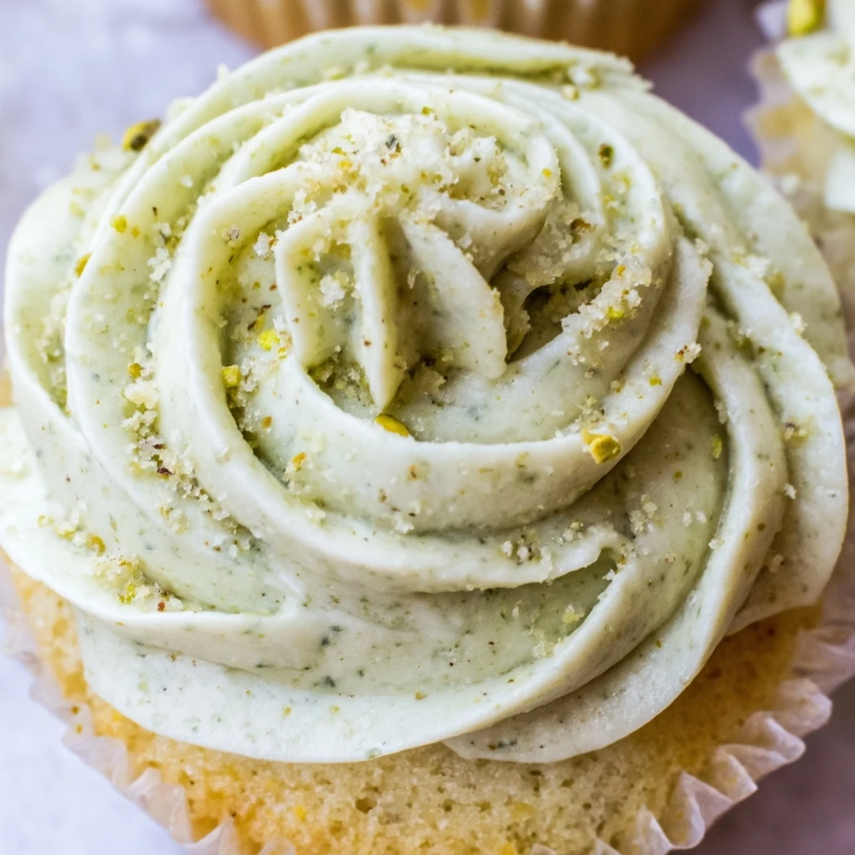 Tender pistachio cupcakes topped with swirls of creamy green buttercream frosting on a rustic plate