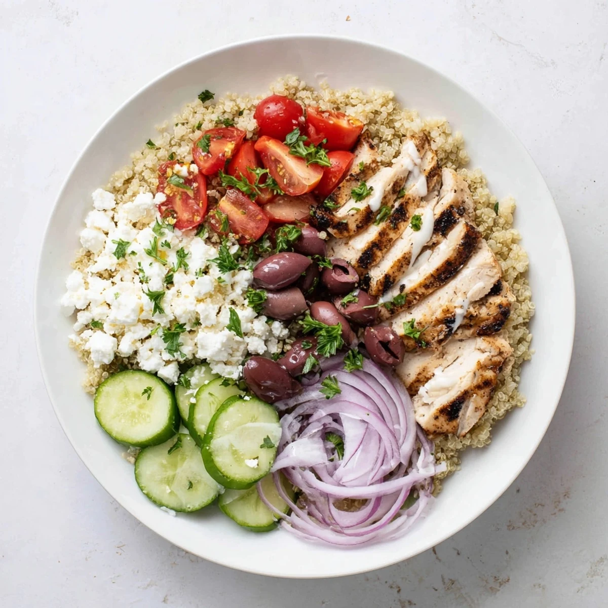 Golden grilled chicken tops a Mediterranean chicken quinoa bowl with crisp vegetables and crumbled feta cheese