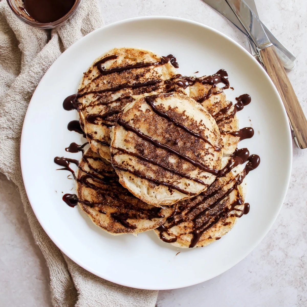 Golden Spanish Churro Pancakes stacked high with rich chocolate sauce drizzled on top