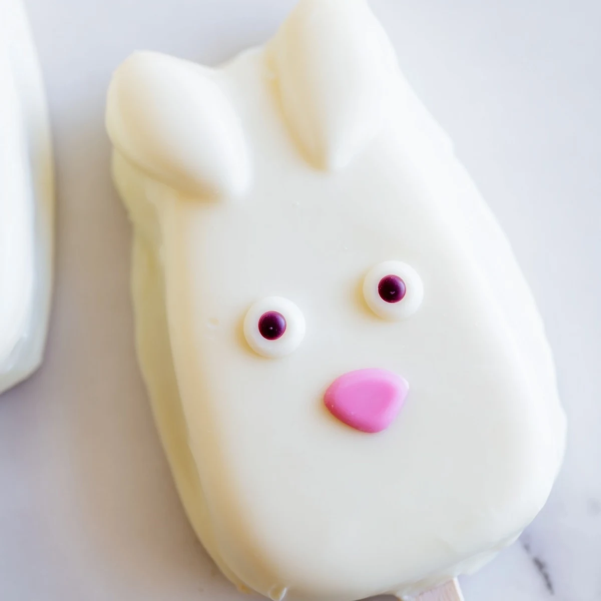 Adorable white chocolate bunny cakesicles decorated with candy eyes on a festive Easter dessert tray.