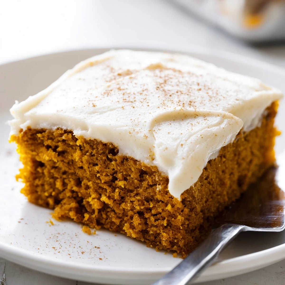 Moist pumpkin bars with cream cheese frosting sliced and plated on a rustic cutting board