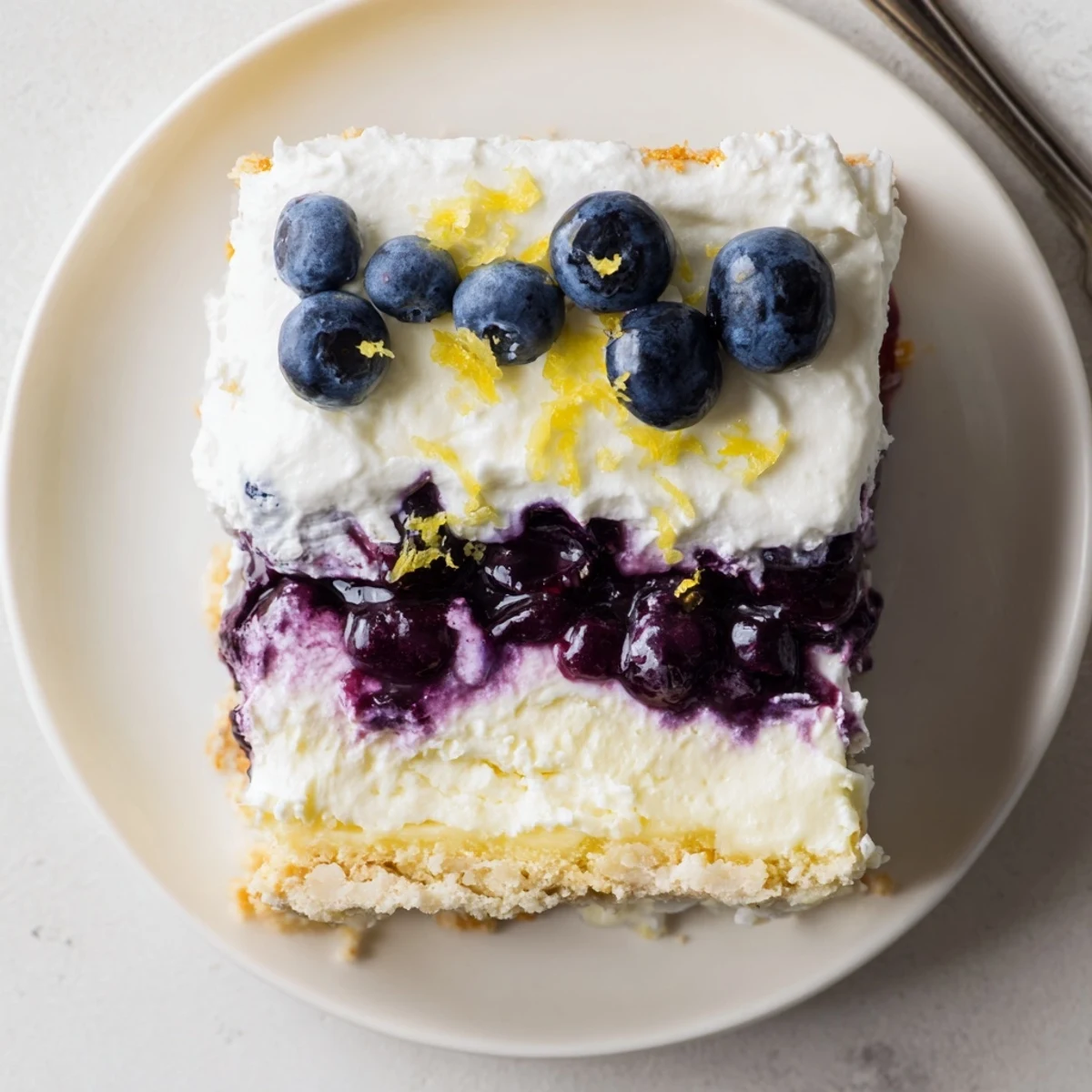 A tall square of lemon blueberry lasagna revealing creamy and fruity layers inside