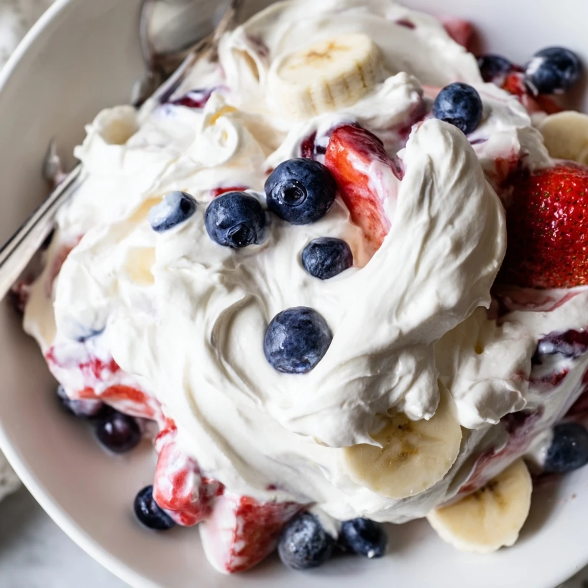 Chilled Red White And Blue Cheesecake Salad studded with strawberries, blueberries, sliced bananas