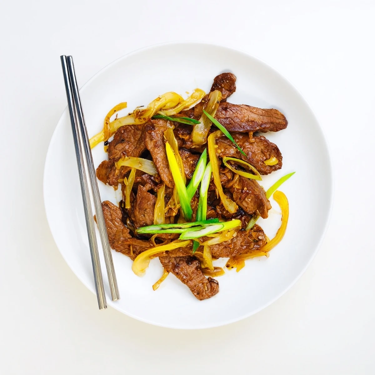 Tender seared flank steak and sweet onions plated steaming hot with fresh green onion garnish