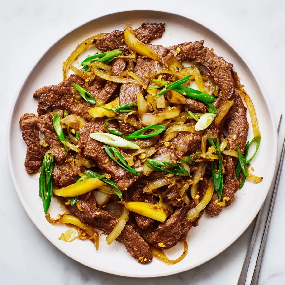 Chinese-style beef stir fry featuring crispy meat slices and wilted onions in glossy brown glaze