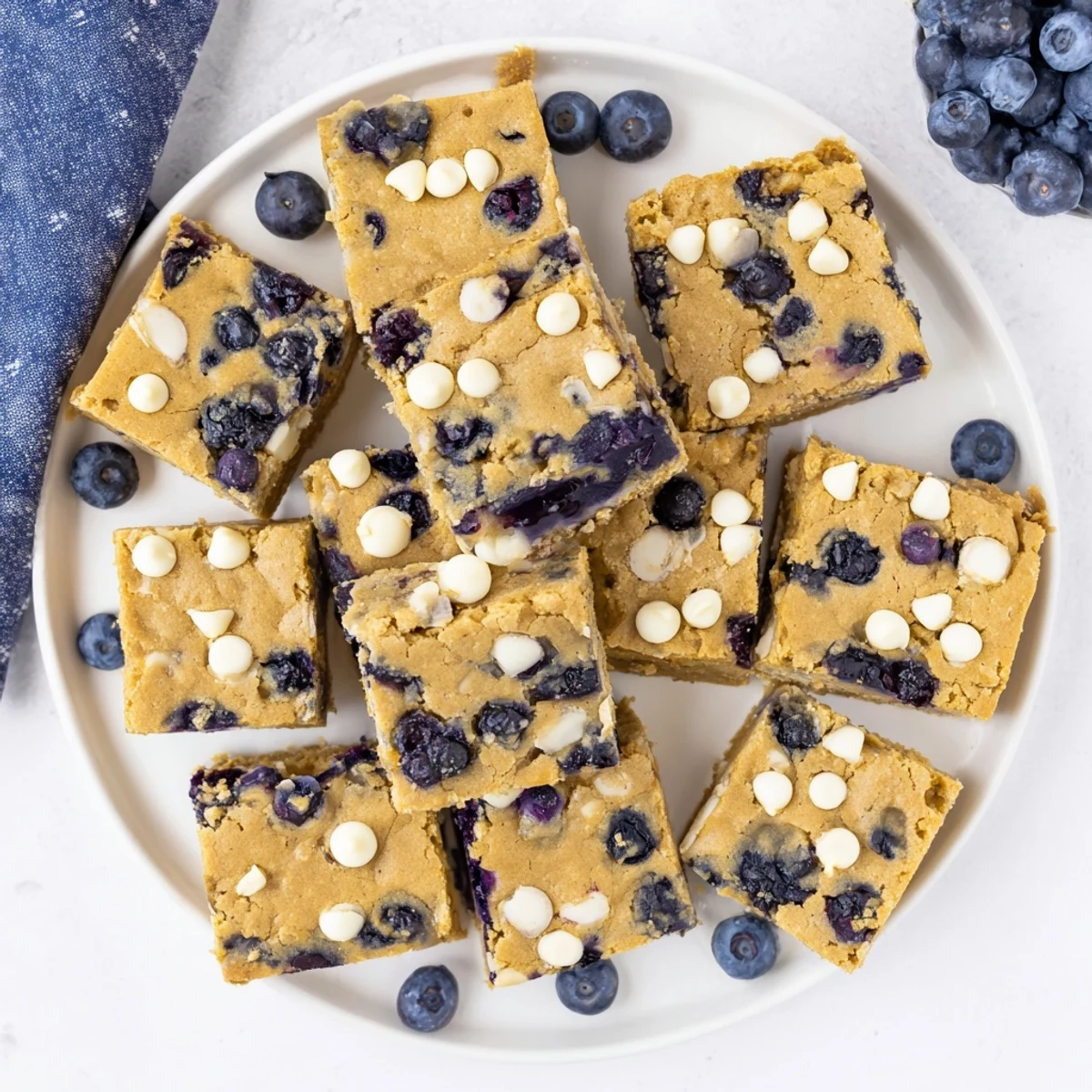 Chewy vanilla blueberry blondies topped with fresh berries on white plate
