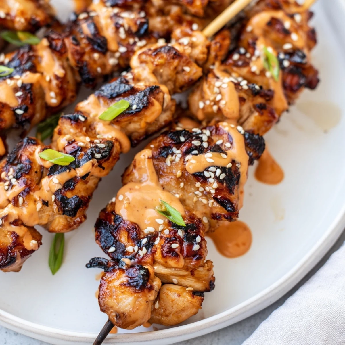 Bang Bang Chicken Skewers glistening with creamy spicy sauce, sesame seeds, spring onions