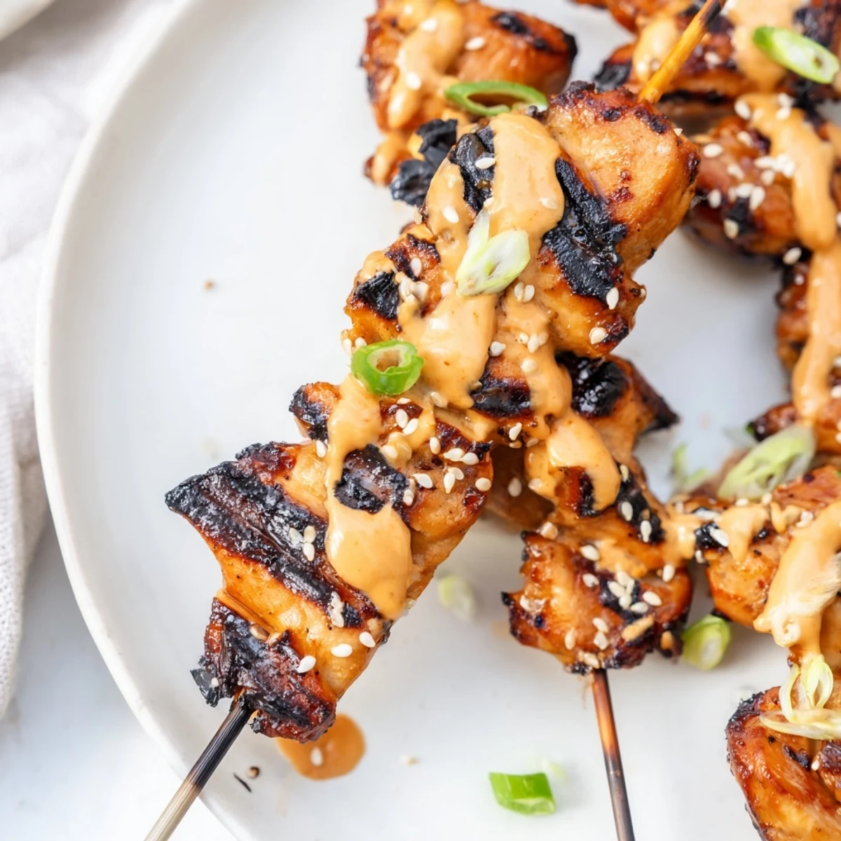 Charred Bang Bang Chicken Skewers on a platter, extra sauce in ramekin