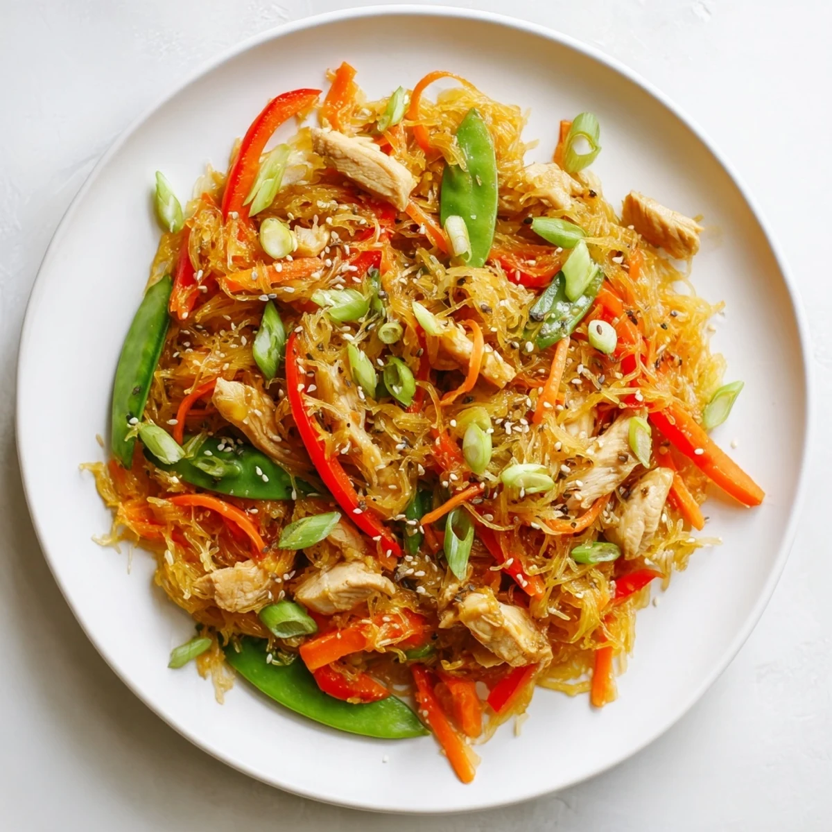 Savory gluten-free spaghetti squash chicken chow mein tossed with crisp vegetables and sesame seed garnish on wooden table