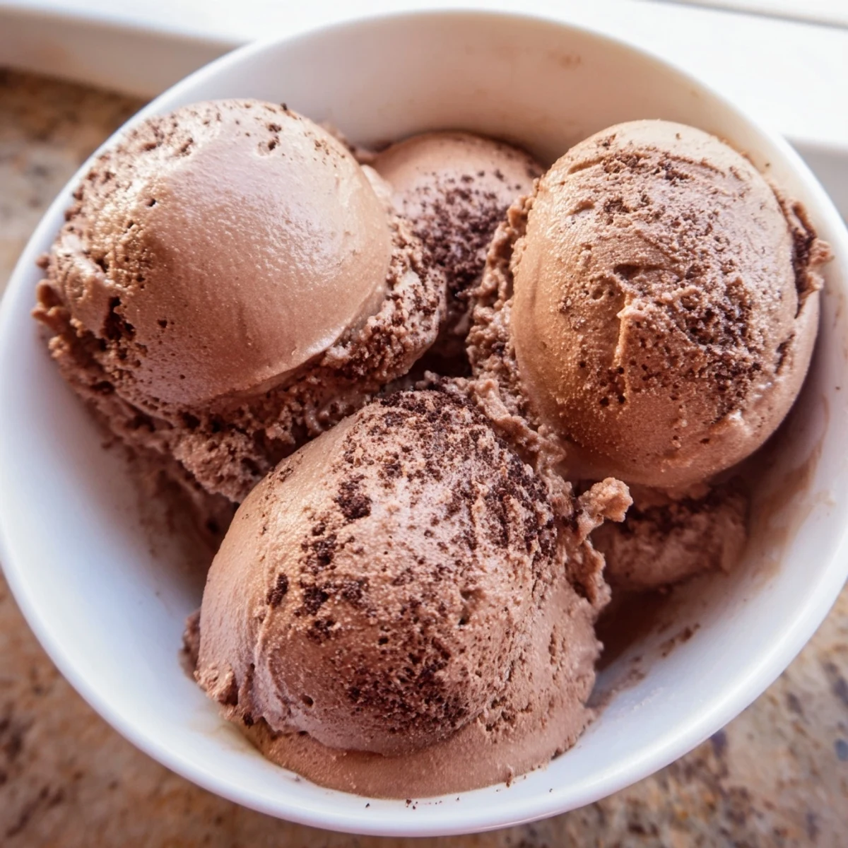 Dark chocolate sourdough ice cream garnished with sea salt flakes and fresh raspberries on a marble surface