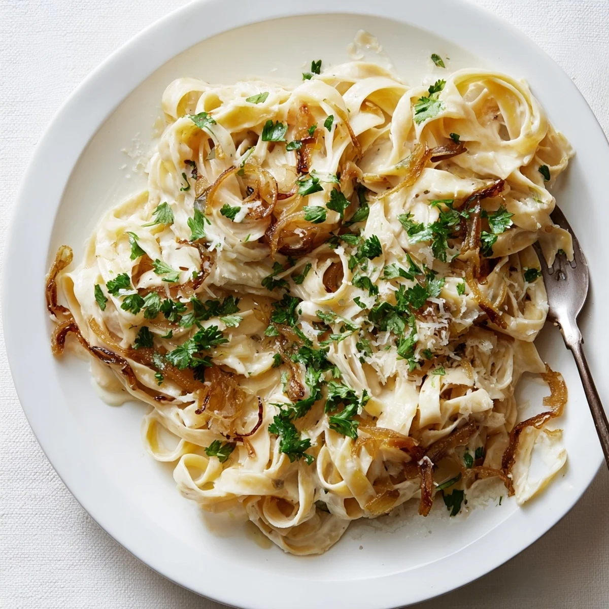 Plates of caramelized onion cream pasta featuring tender noodles in a velvety white sauce topped with Parmesan