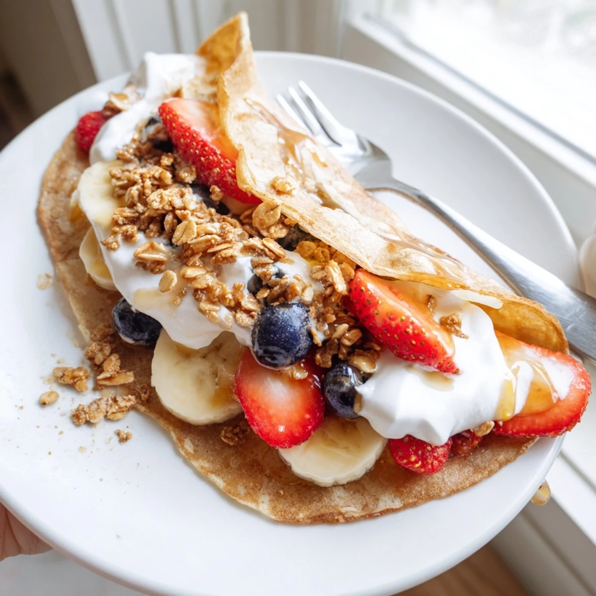 Fluffy pancake tacos filled with fresh strawberries and drizzled maple syrup on a white plate